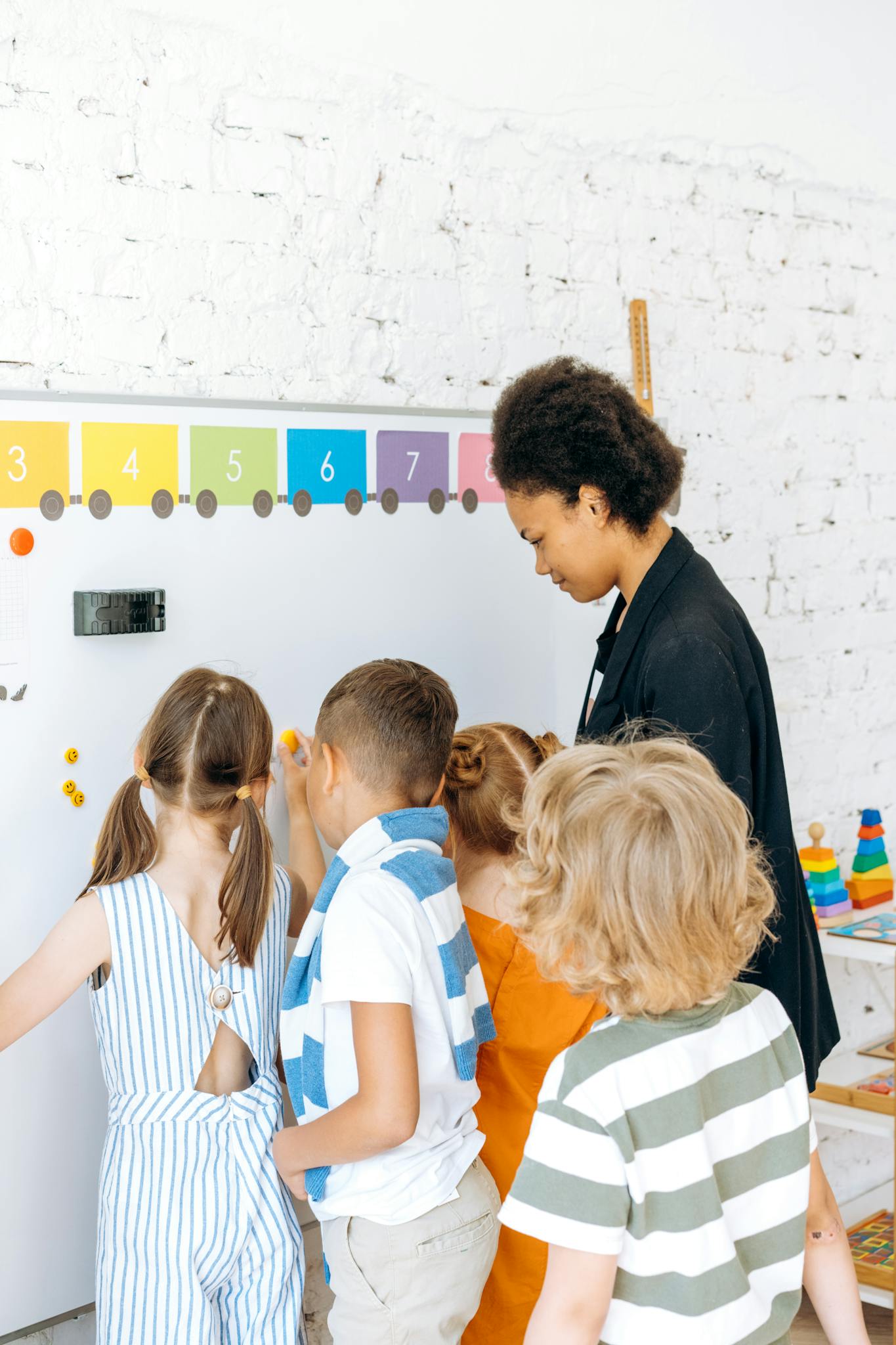 Children engaged in learning with a teacher at a colorful classroom whiteboard.